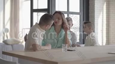 可爱的儿子拥抱疲惫的妈妈站在室内的桌子旁。 兄弟<strong>情谊</strong>。 家庭关系。